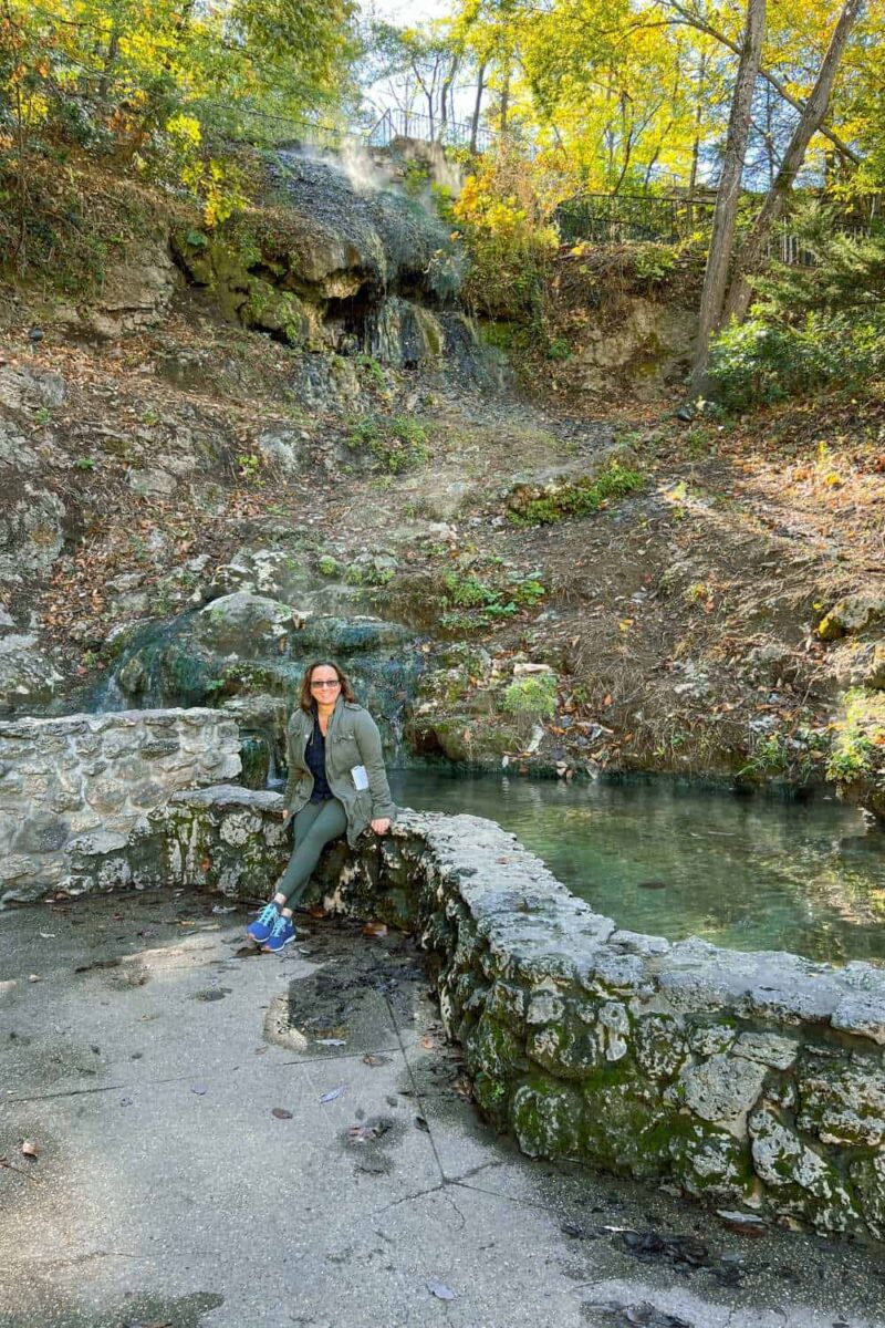 woman sitting on stone path at hot water cascade in hot springs national park