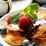poffertjes covered with syrup and berries on a white platter