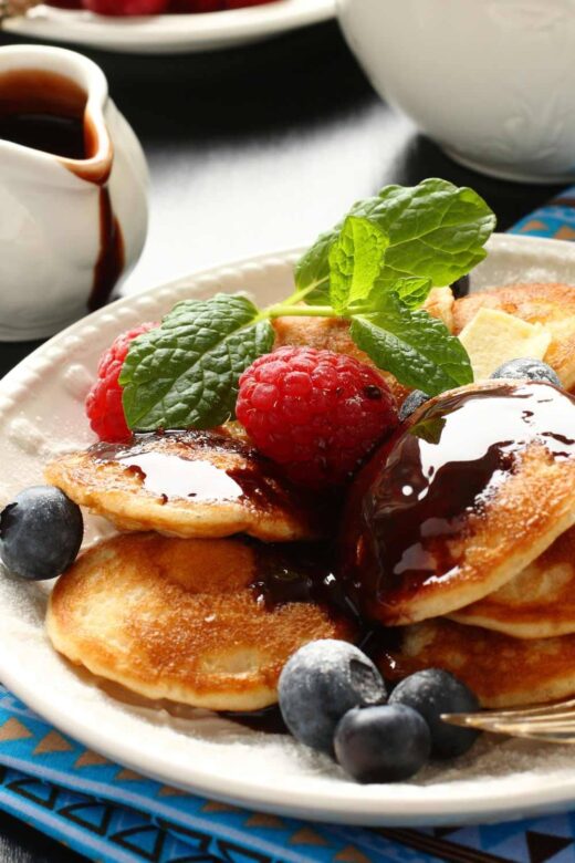 poffertjes covered with syrup and berries on a white platter
