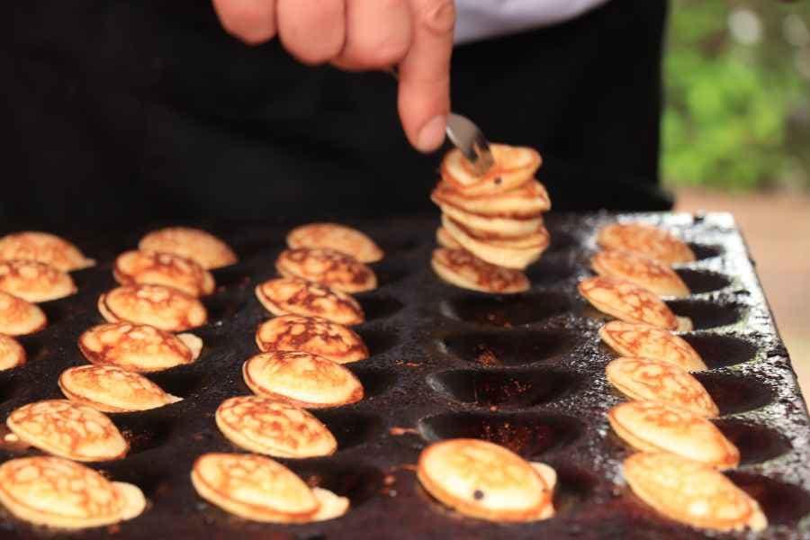 woman taking dutch mini pancakes out of poffertjes pan with fork