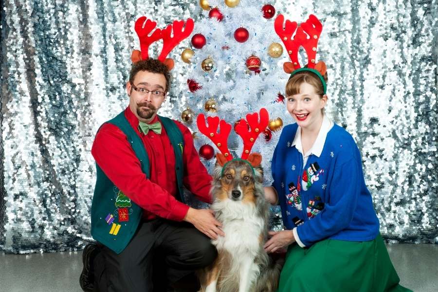 man woman and dog dressed up in ugly christmas sweaters and antlers
