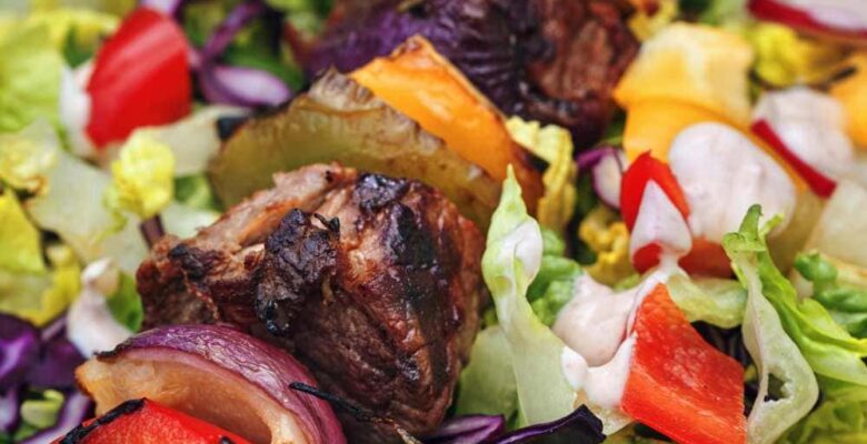 beef shish kebabs on skewer on platter of fresh green salad