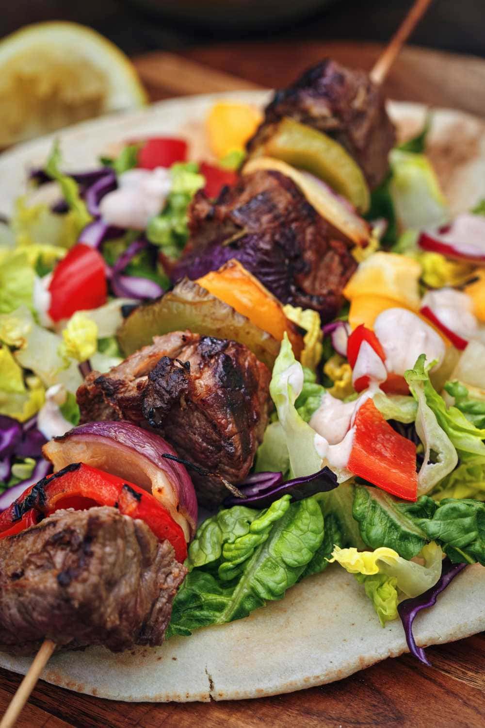 beef shish kebabs on skewer on platter of fresh green salad