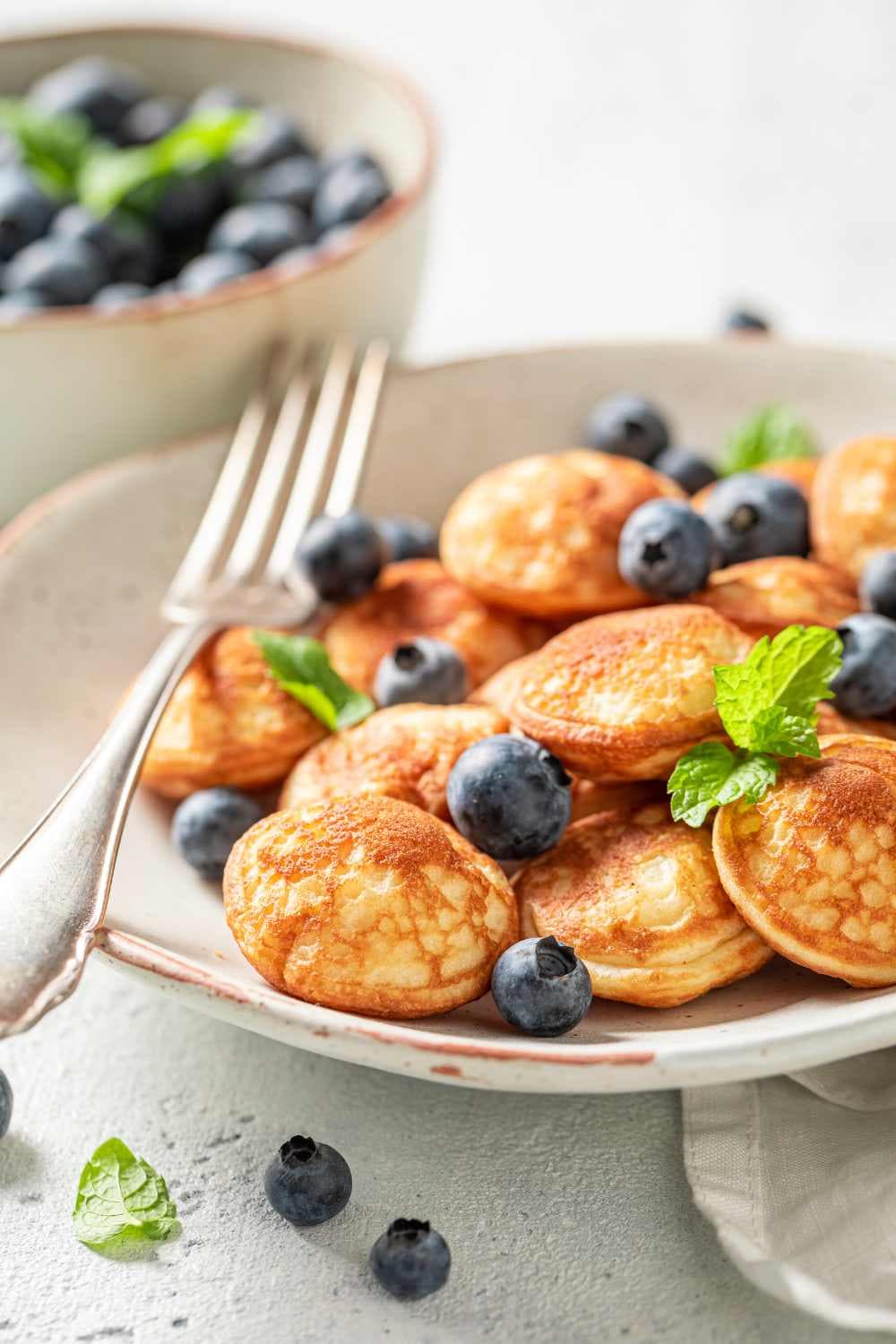 poffertjes on white platter with berries and mint sprigs