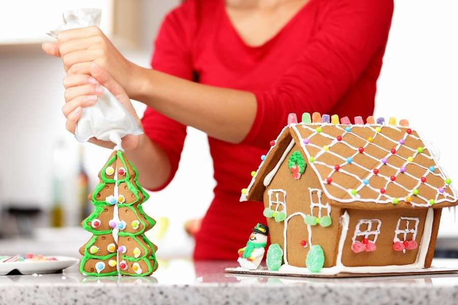 woman putting icing on gingerbread house
