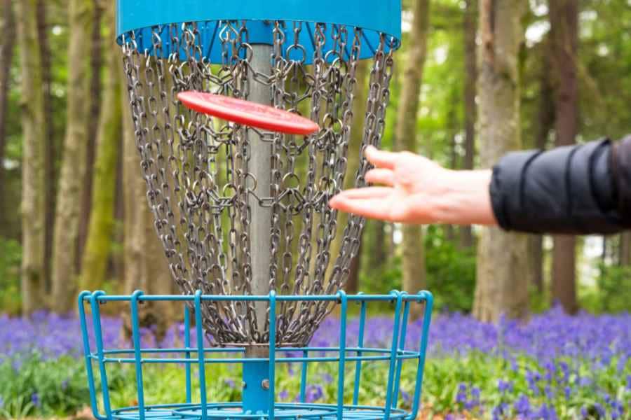 person throwing a disk at the chain basket for frisbee golf