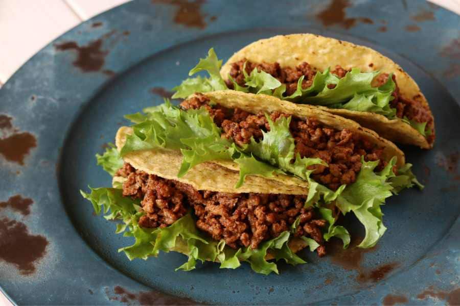 three homemade tacos with lettuce on a rustic blue plate