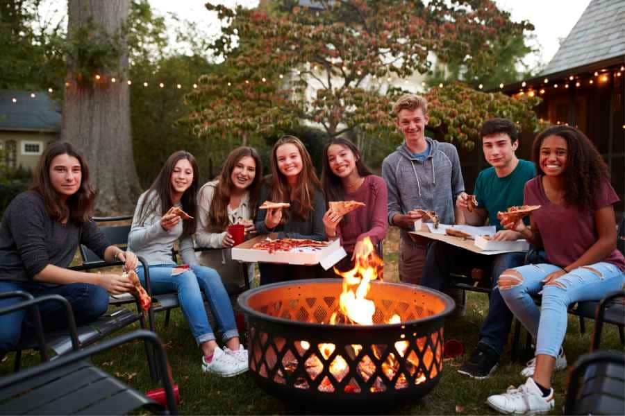 teens sitting in backyard around firepit eating pizza