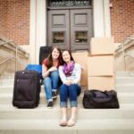 two college freshman moving into residence hall with luggage and boxes