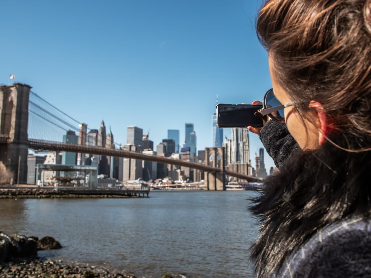 Teen girl taking picture of Manhattan from DUMBO