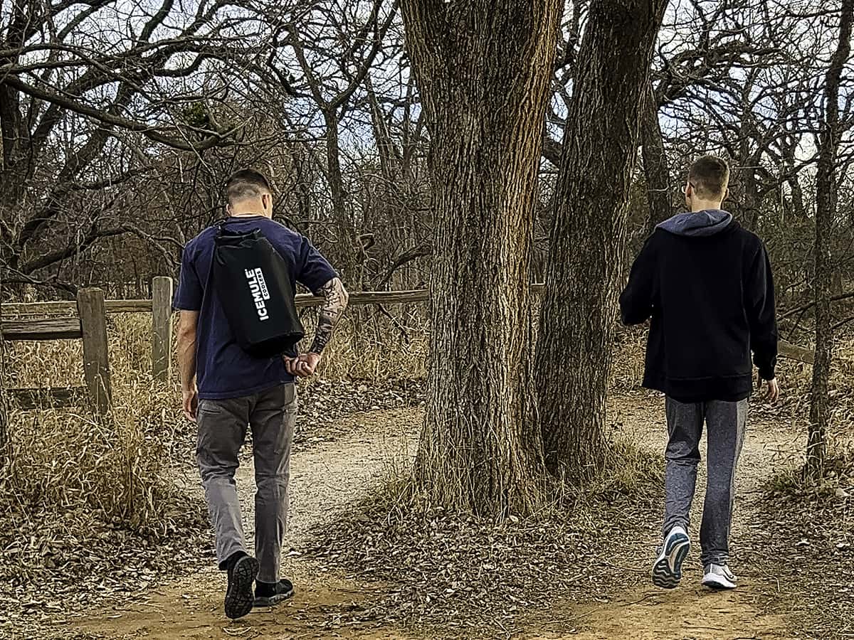 boys walking in woods with one having a cooler backpack on back