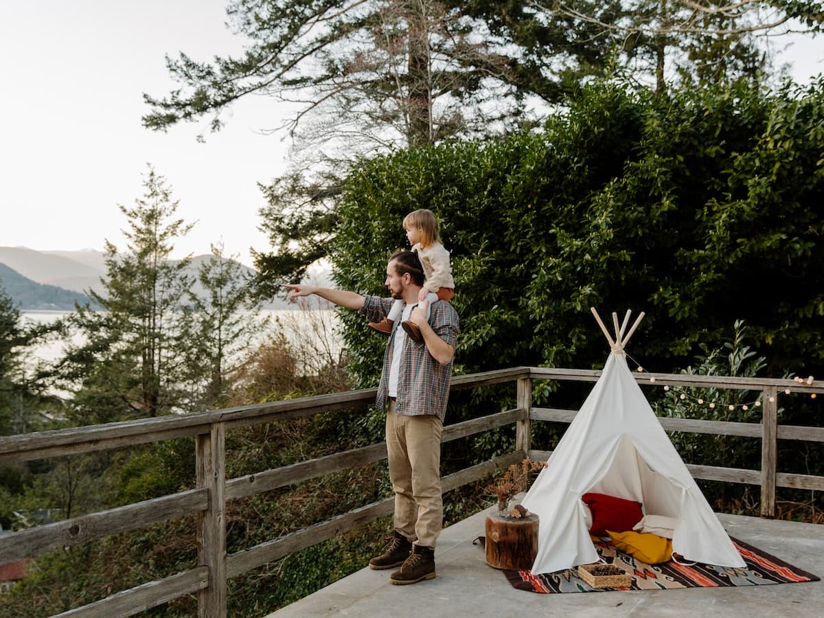 man and child looking at water next to teepee tent