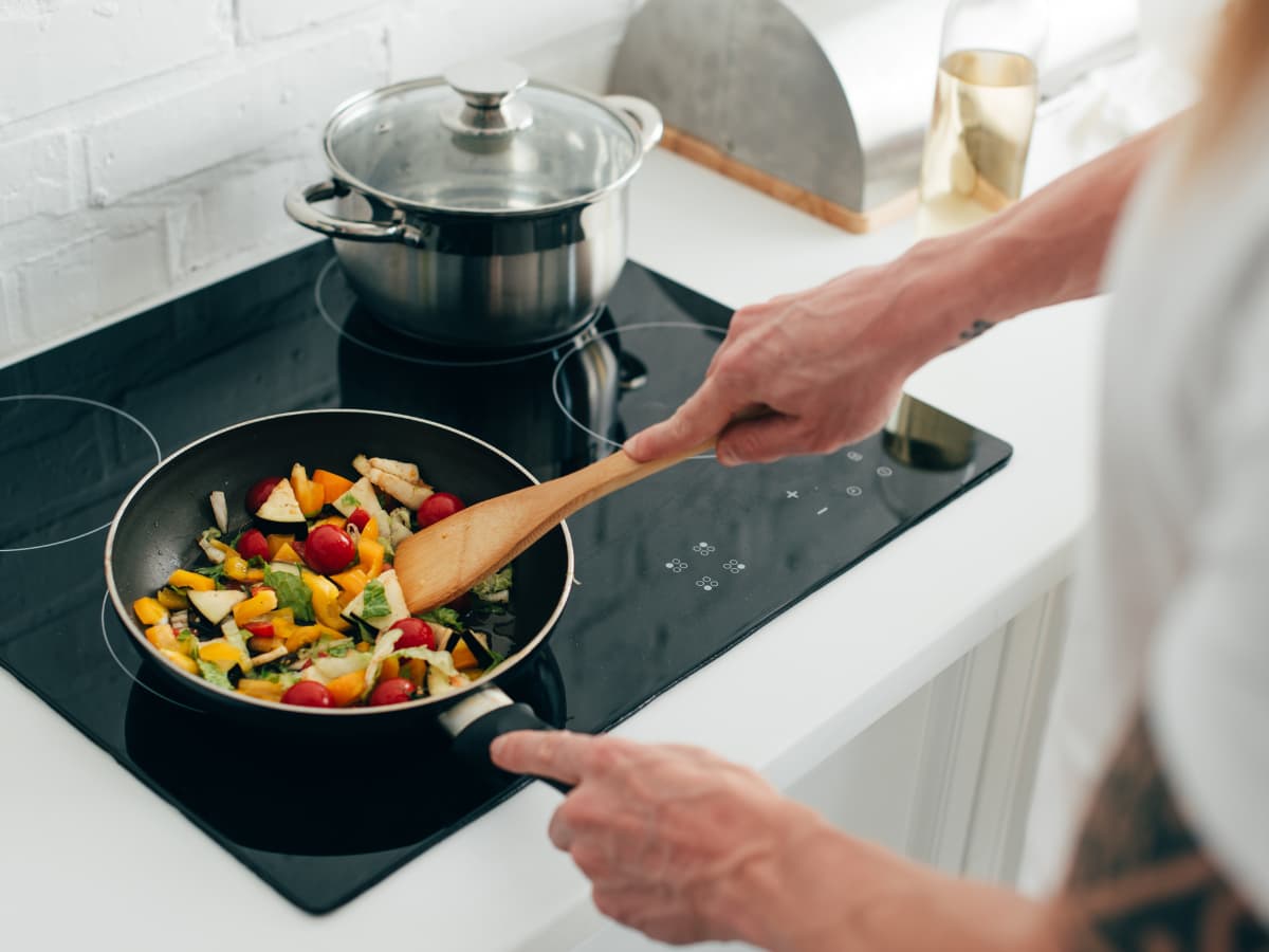 cook sauteeing vegetables in stove top pan