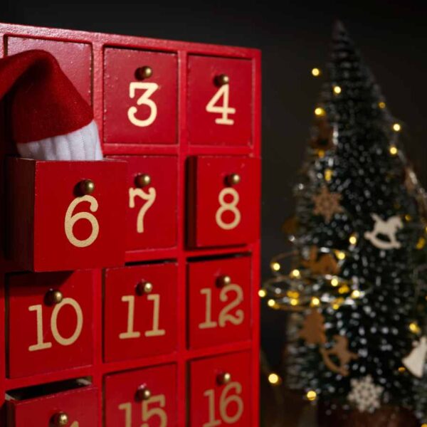 red wooden advent calendar with christmas tree and lights in background