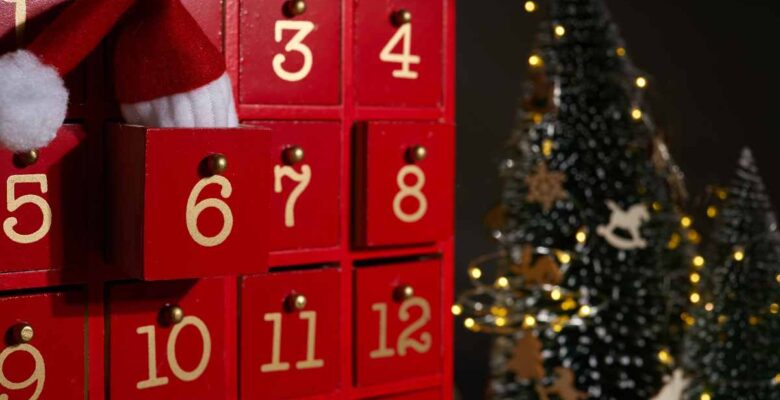 red wooden advent calendar with christmas tree and lights in background