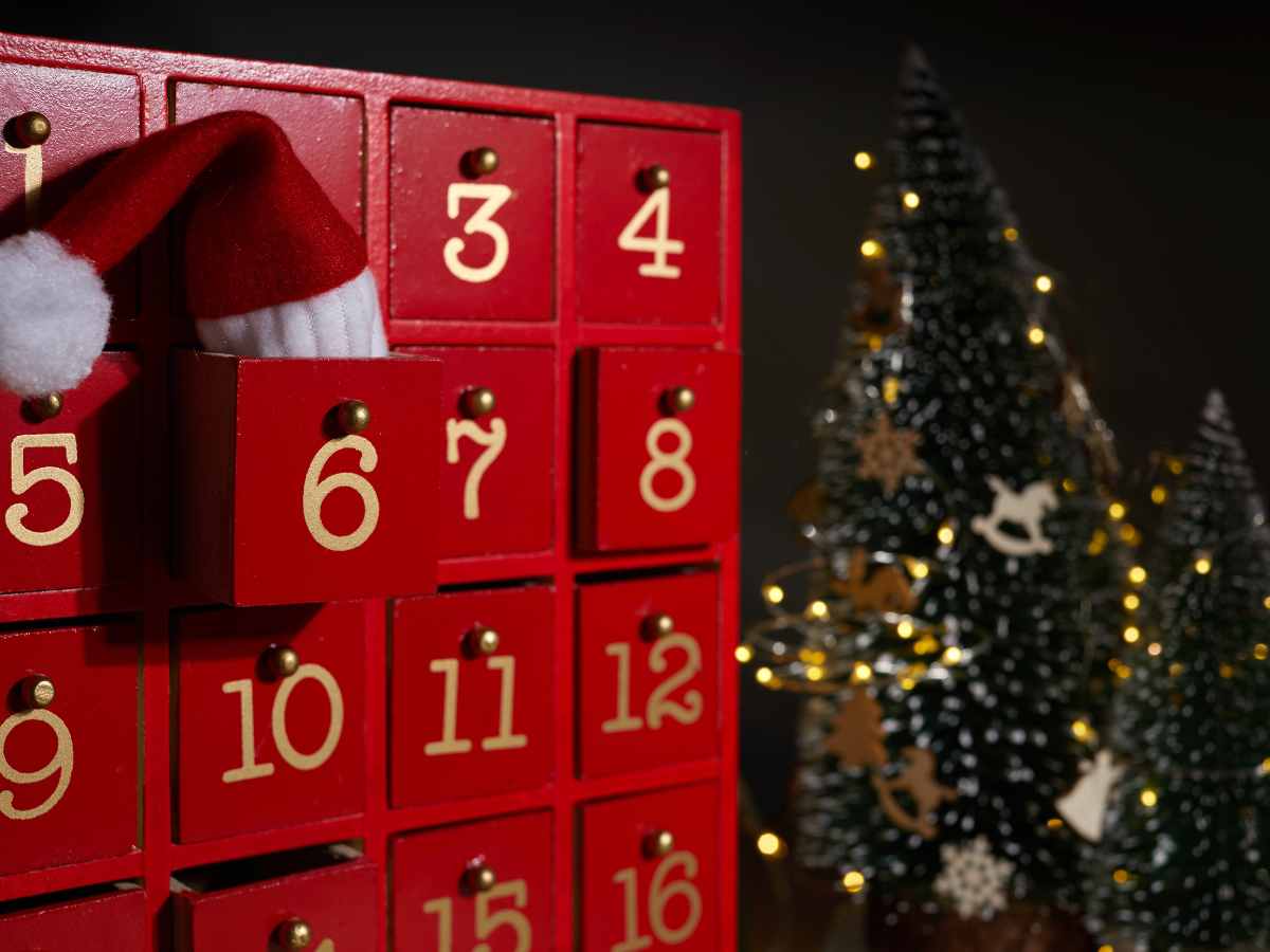 red wooden advent calendar with christmas tree and lights in background