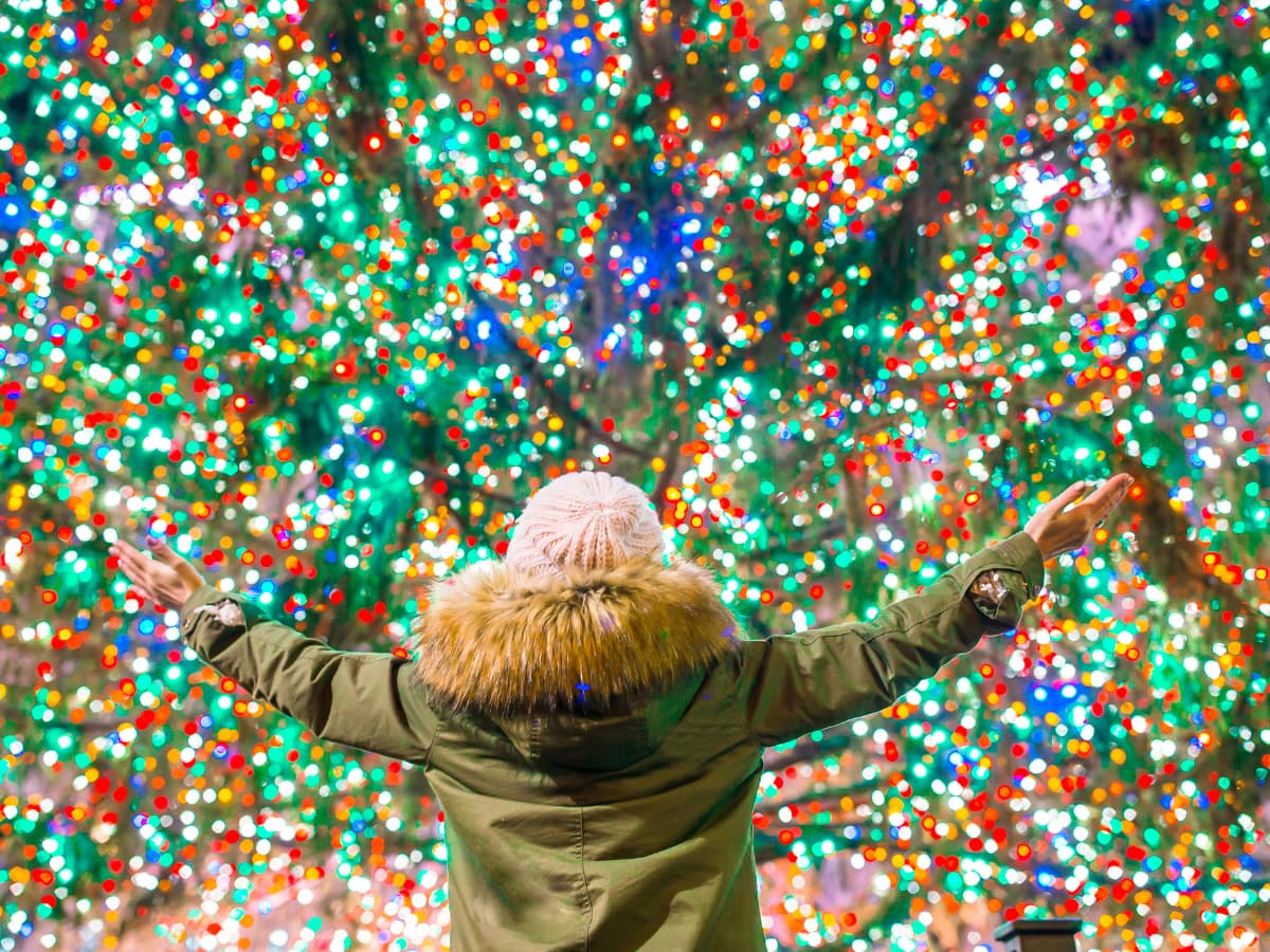 person with arms outstretched infront of Rocerfeller Center Christmas Tree