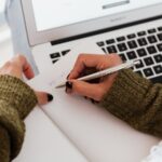 writing into a jourmal over a laptop