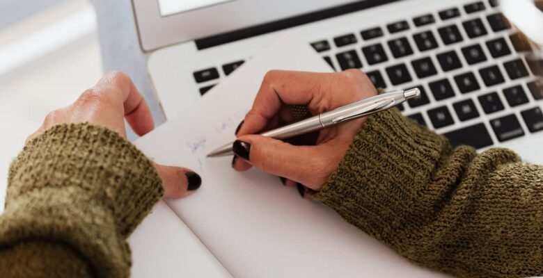 writing into a jourmal over a laptop