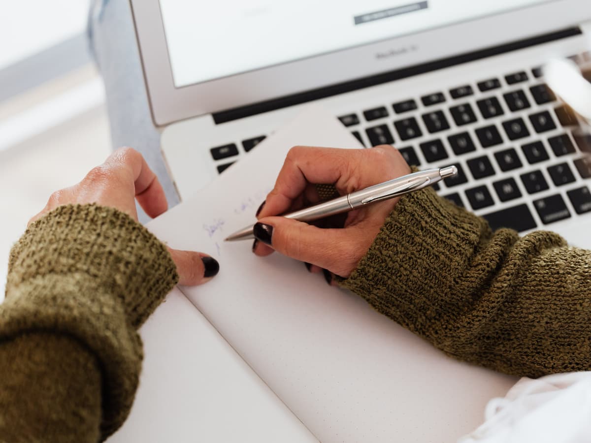 writing into a jourmal over a laptop