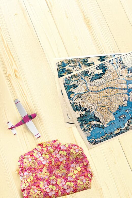 flatlay of travel map, book, plane, and floral shirt