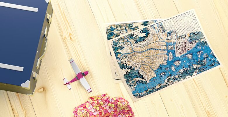 flatlay of travel map, book, plane, and floral shirt