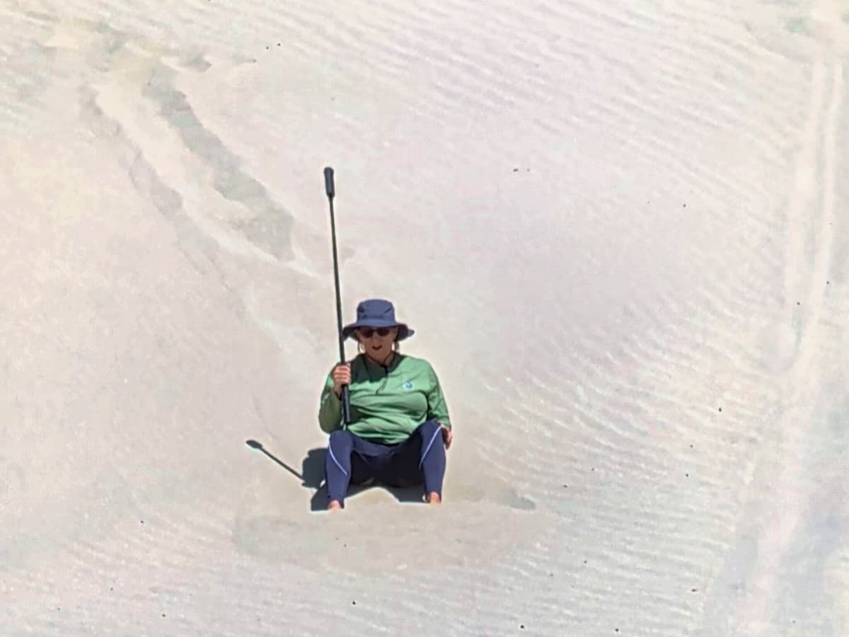 woman sitting in sand with 360 camera on tripod