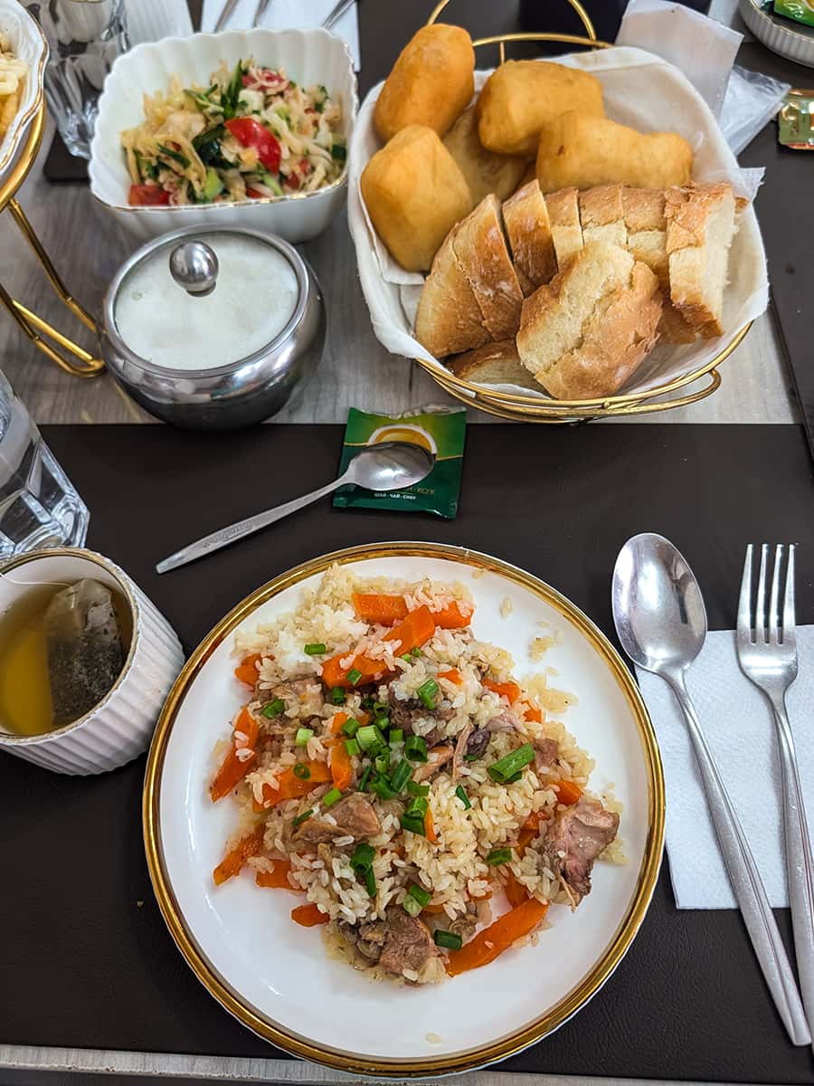 table setting with Plov or rice pilaf on the plate, bread basket, and hot tea