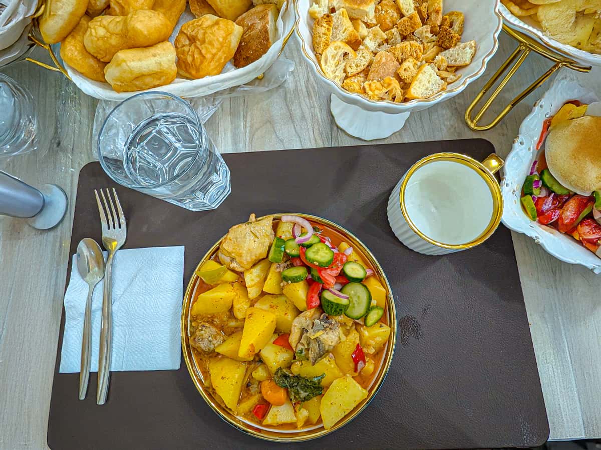 table setting with meat and potatoes on plate, bread basket, salad and hot tea