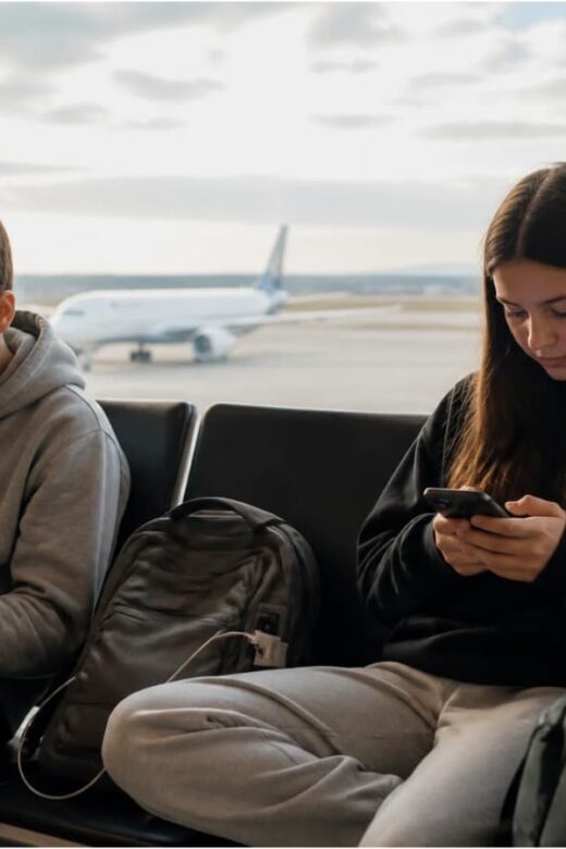 Two teenagers using smartphones at an airport gate, illustrating digital safety for family travel